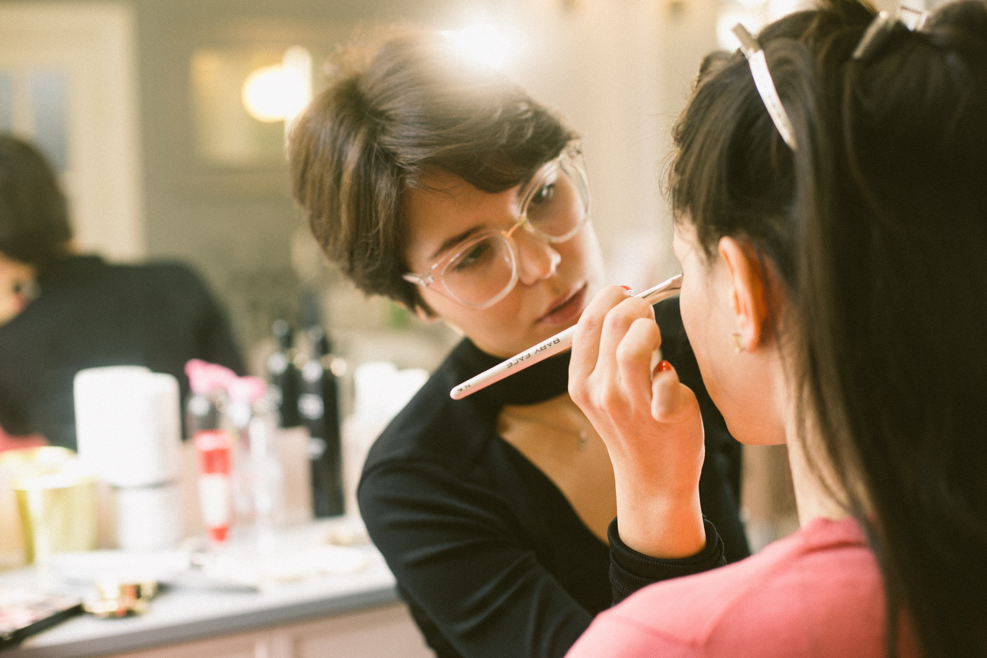 Young visagiste applying makeup on model